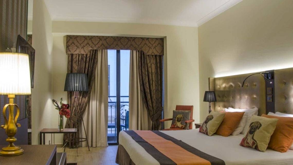 Zimmer im AX The Victoria Hotel mit Bett, Lampen und Balkon.