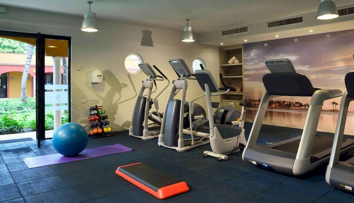 Fitnessraum im Catalonia Playa Maroma Hotel mit Laufbändern, Hanteln und einer großen Kugel.
