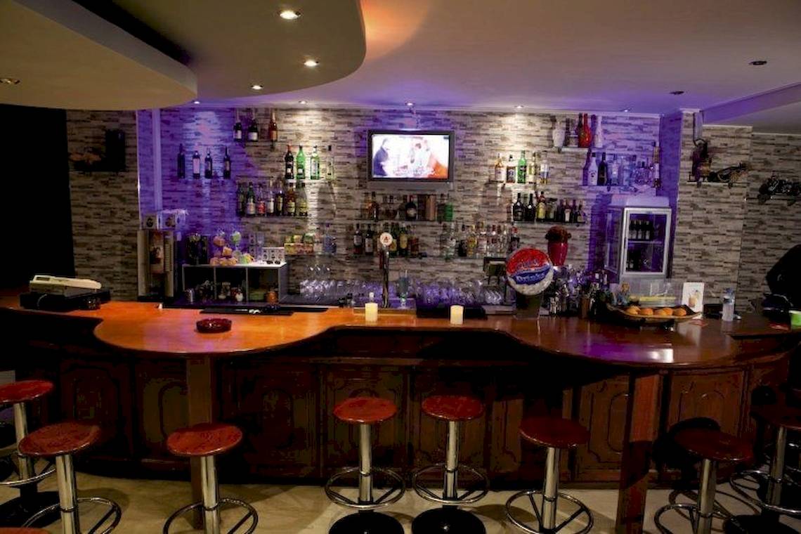 Innenansicht der Bar im Sunny Days Hotel mit einer Theke, roten Stühlen, vielen Flaschen und einem Fernseher