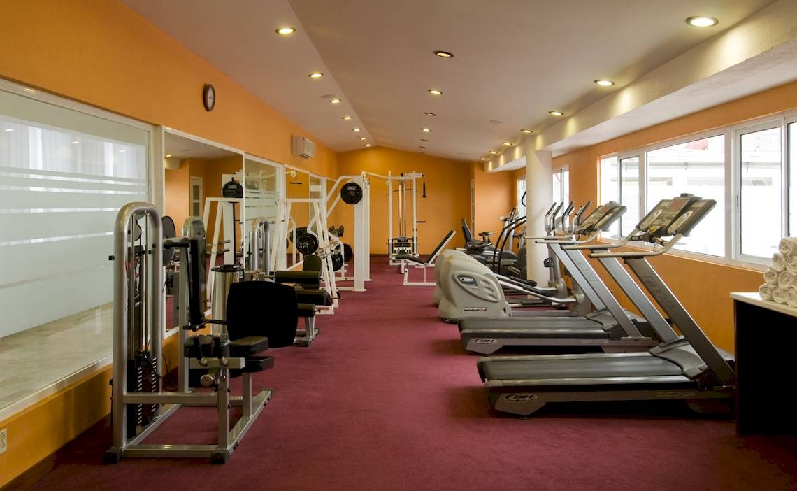 Fitnesscenter im Ocean Maya Royale Hotel mit roten Teppichboden, Fitnessgeräten und Fenstern.