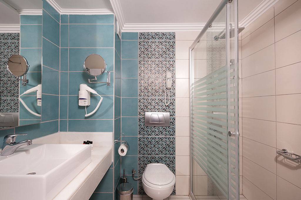 Badezimmer des Side Aluna Hotels mit blauen Fliesen, Dusche, Toilette und Waschbecken.