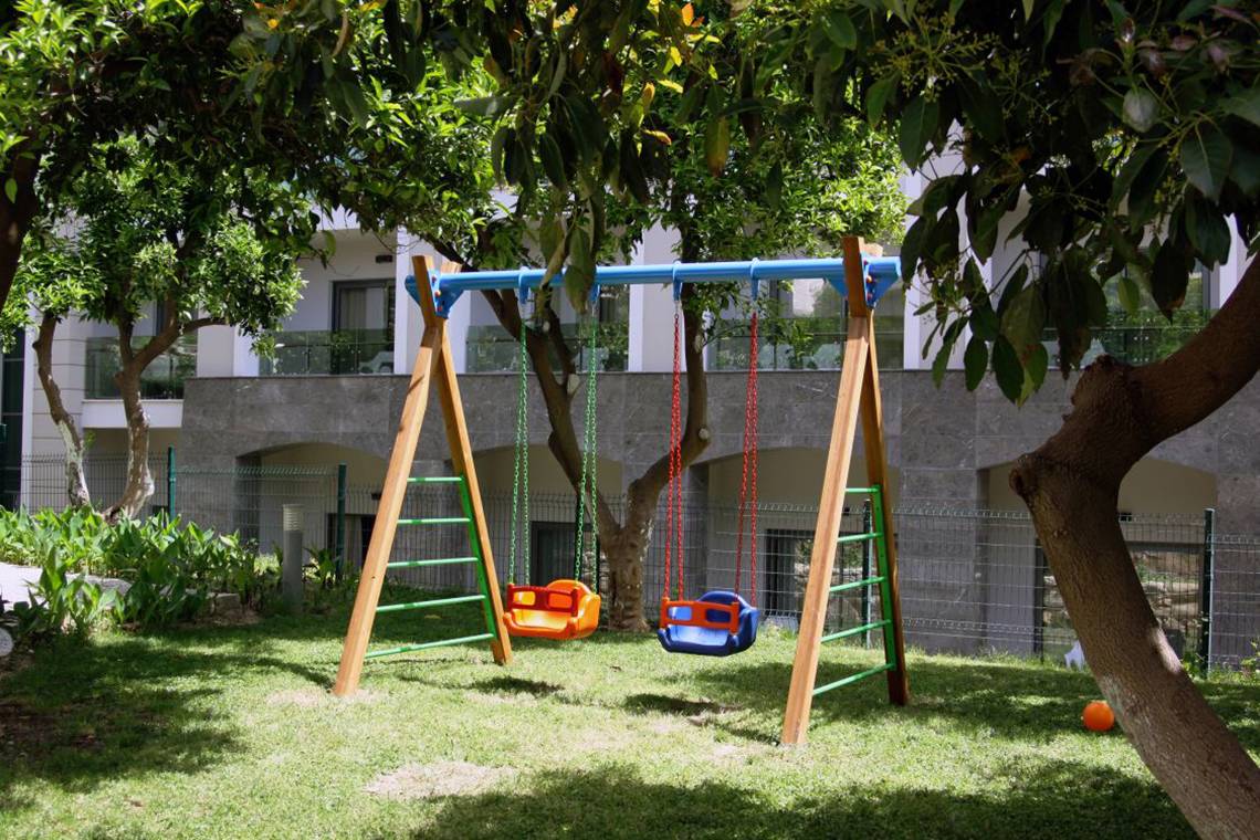Zwei Kinderschaukeln unter Bäumen im Garten des Horus Paradise Luxury Resort.