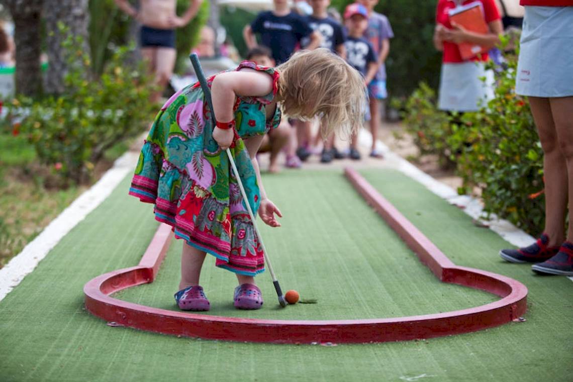 Ein kleines Mädchen spielt Minigolf auf einem grünen Platz im Freien.