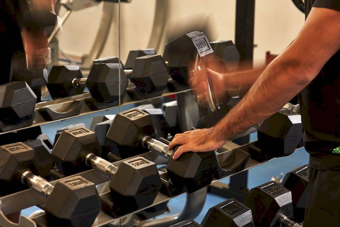 Mann im Fitnessstudio benutzt Hanteln in einem Spiegel