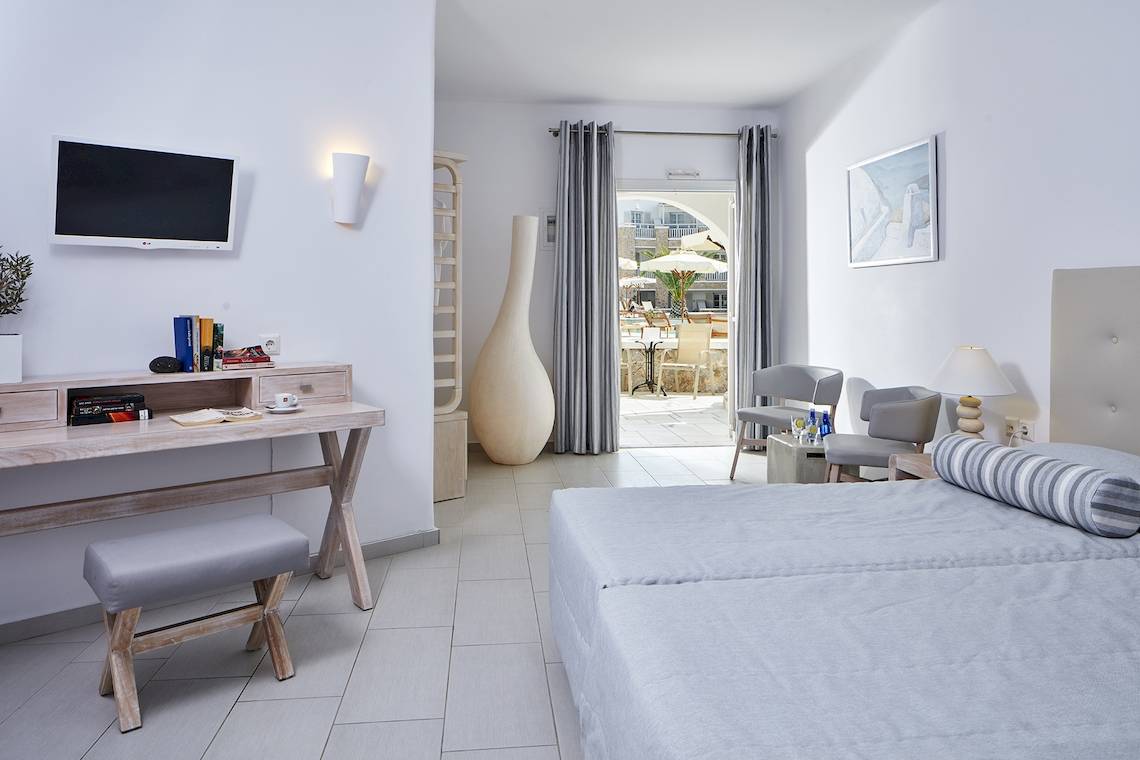 Hotelzimmer mit einem Bett, Schreibtisch, Fernseher, Stühle, Vase und Balkonzugang.