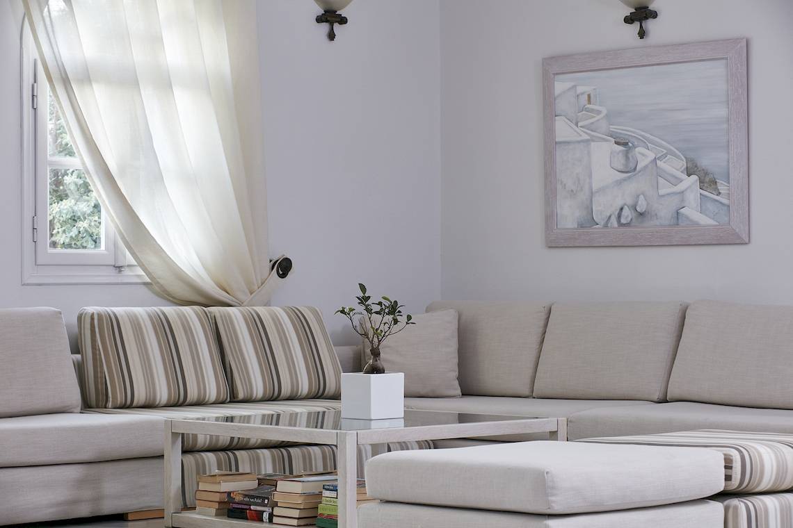 Wohnzimmer mit grauem Sofa, Couchtisch mit Büchern und einer Pflanze, neben einem Fenster mit Vorhang.