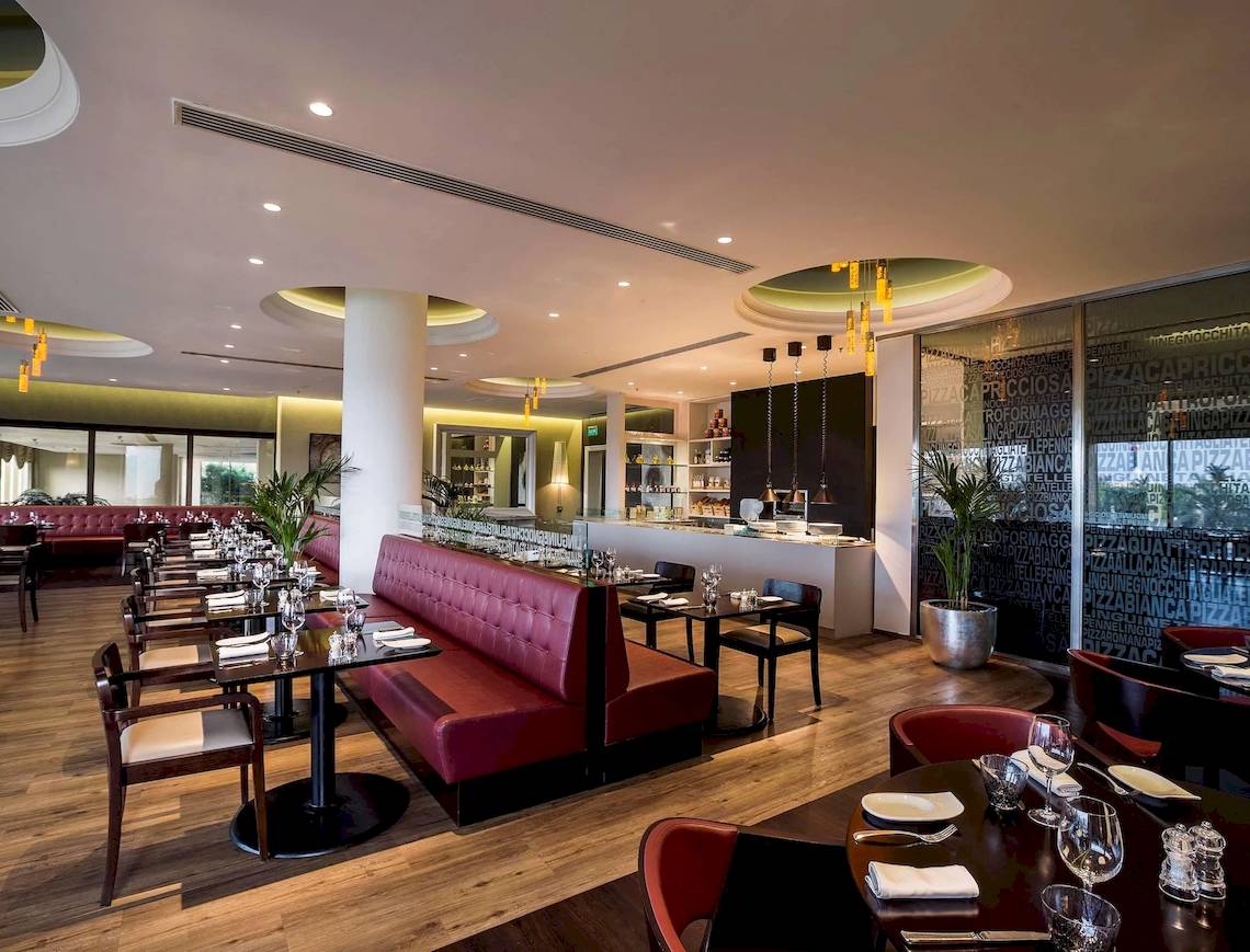 Innenansicht des Restaurants im Radisson Blu Hotel & Resort, Abu Dhabi mit roter Bestuhlung und Holzboden.