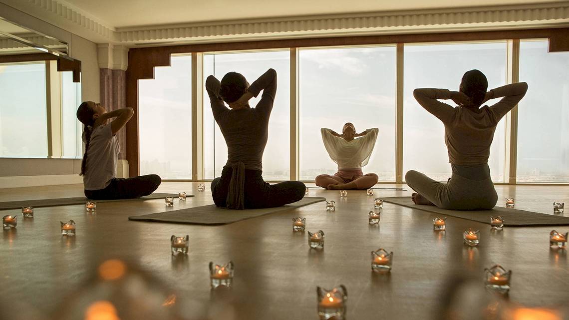 Yoga-Stunde im Burj Al Arab Jumeirah Hotel mit mehreren Frauen, die vor großen Fenstern praktizieren.