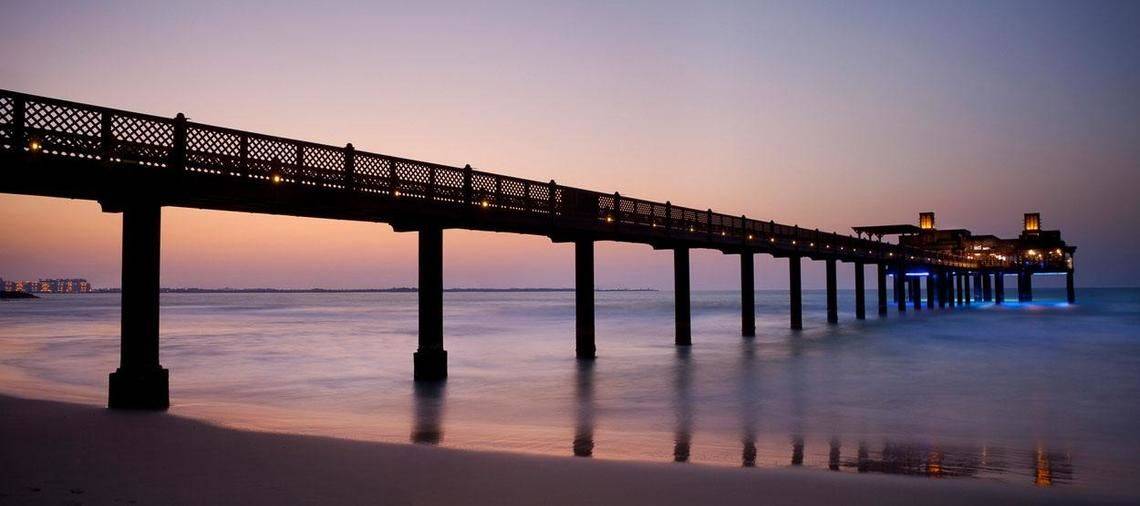 Jumeirah Al Qasr Pier bei Sonnenuntergang mit beleuchteten Säulen und blauem Wasser.