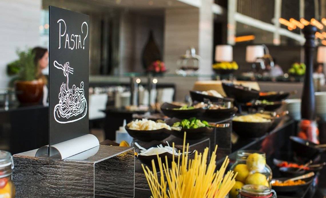 Buffet-Tisch im Pullman Dubai Downtown Hotel mit verschiedenen Speisen und einem Schild, das Pasta anbietet.