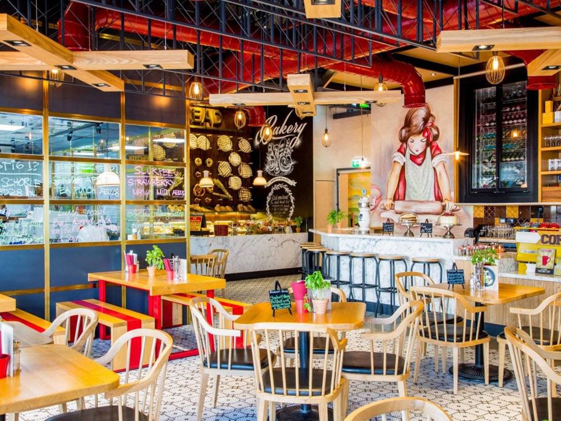 Innenansicht des Restaurants im Pullman Dubai Downtown mit Tischen, Stühlen und einer Wandmalerei.