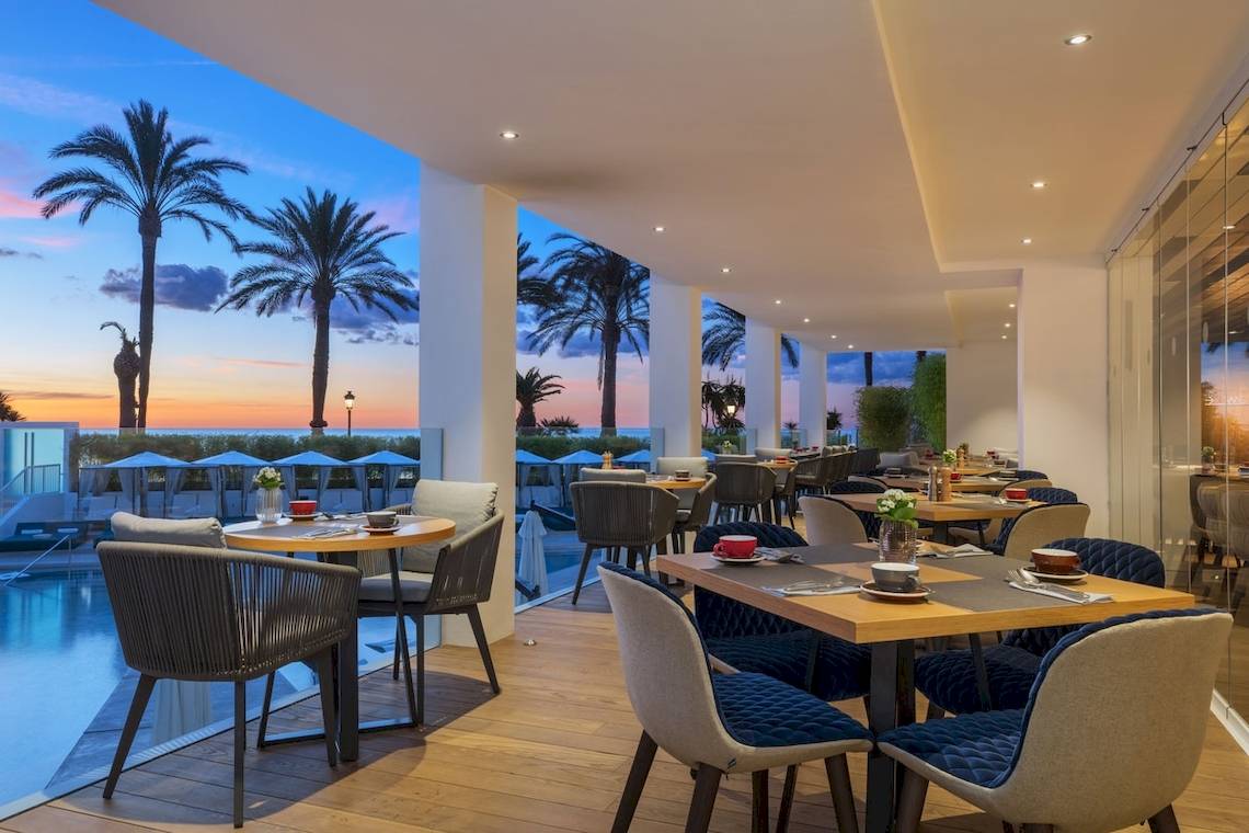 Terrasse des W Ibiza Hotels mit Tischen und Stühlen und Blick auf den Pool und die Palmen