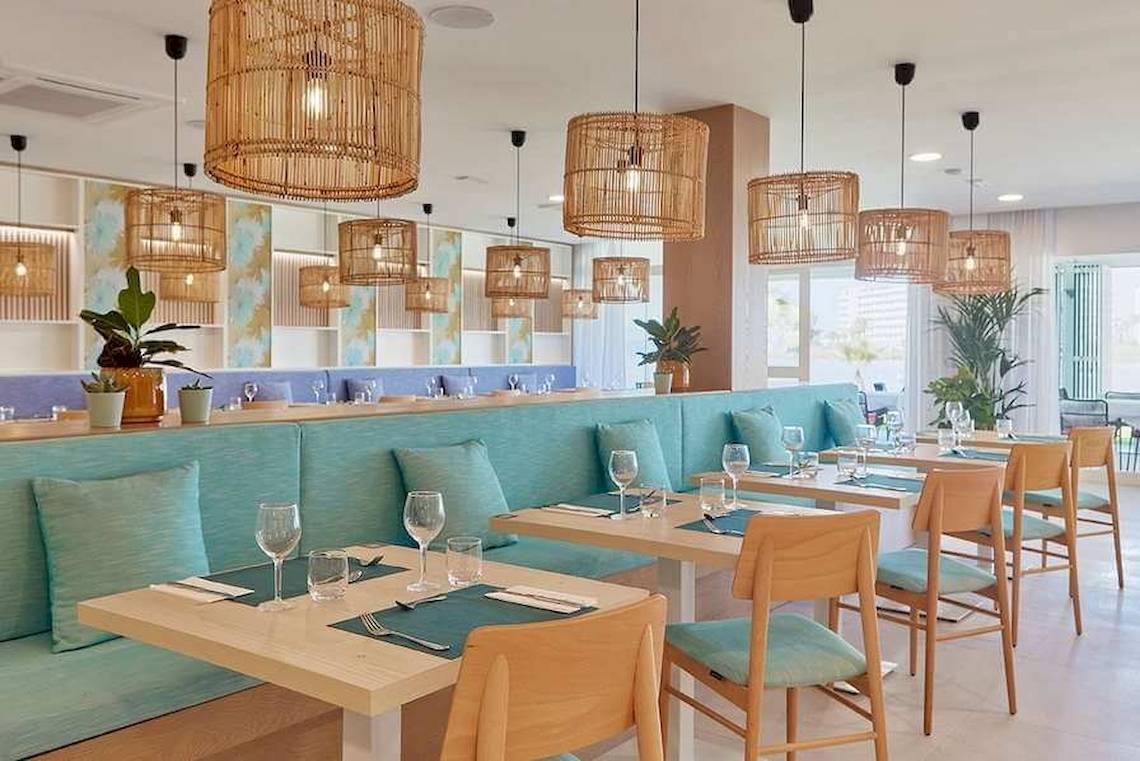 Innenansicht des Restaurants im Universal Aparthotel Elisa mit blauen Sofas und Holztischen.