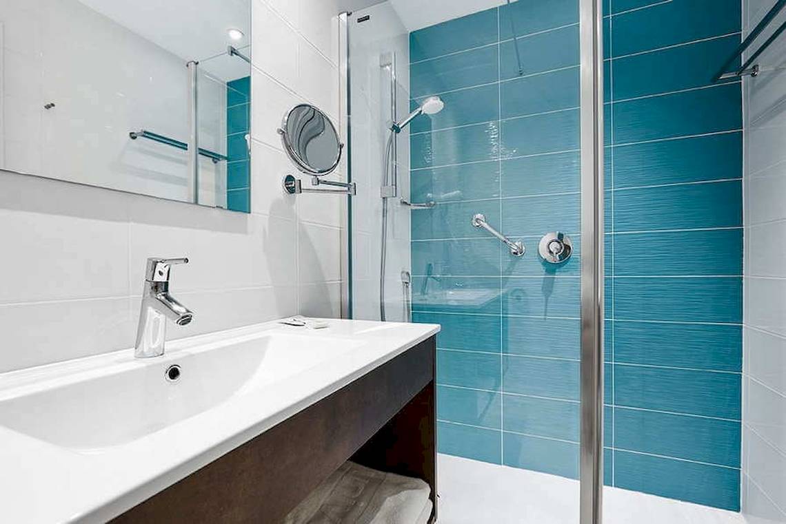 Ein Badezimmer mit blauen Fliesen, einer Duschkabine und einem Waschbecken im Universal Aparthotel Elisa.