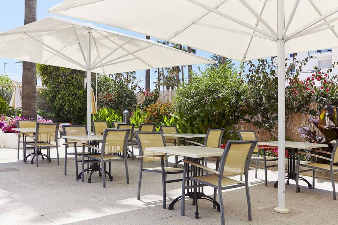 Außenrestaurant-Terrasse mit Tischen und Stühlen unter großen weißen Sonnenschirmen im Bikini Hotel.