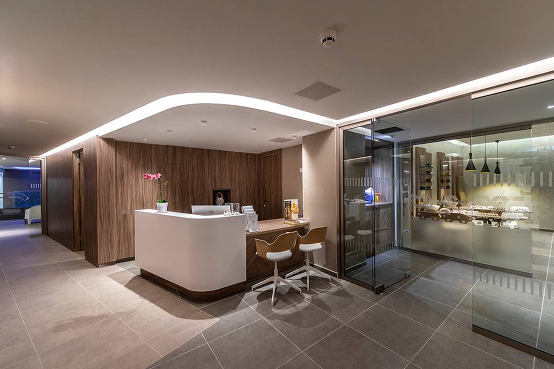 Lobby und Rezeption des Faros Hotel Ayia Napa mit modernem Design, hölzernen Wänden und einem Schreibtisch.