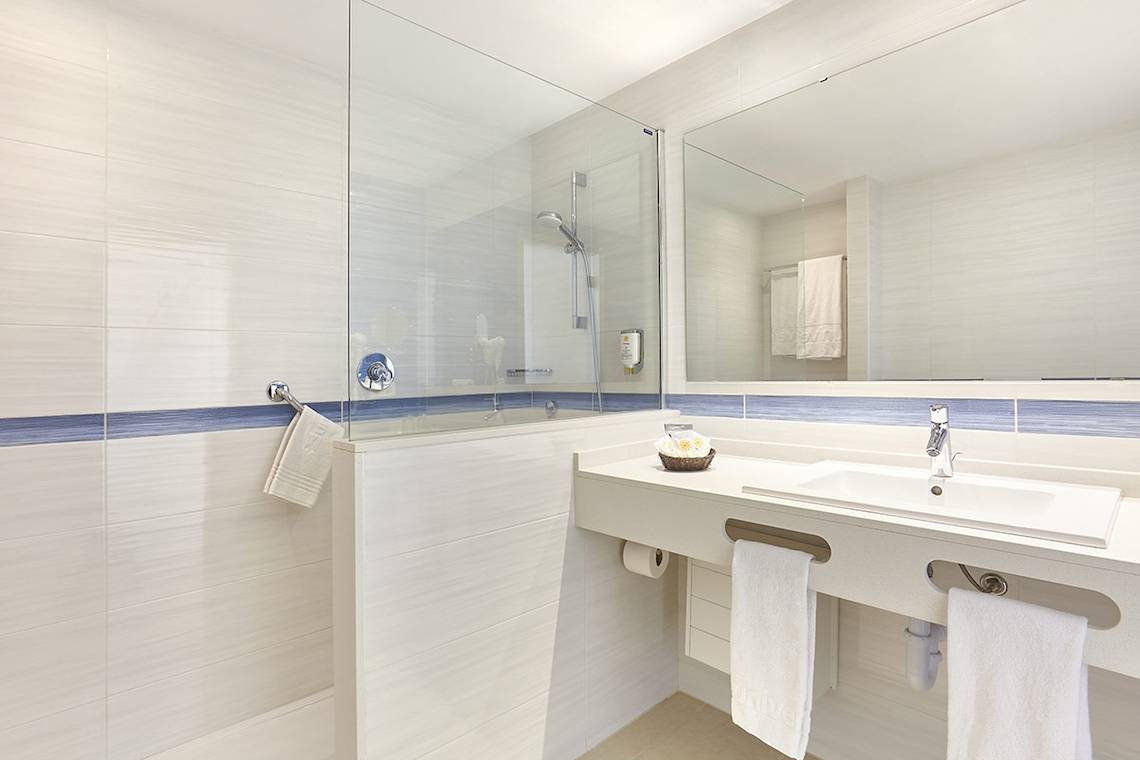 Badezimmer im Lido Park Hotel mit blauer Akzentlinie, Glasdusche und Waschbecken.