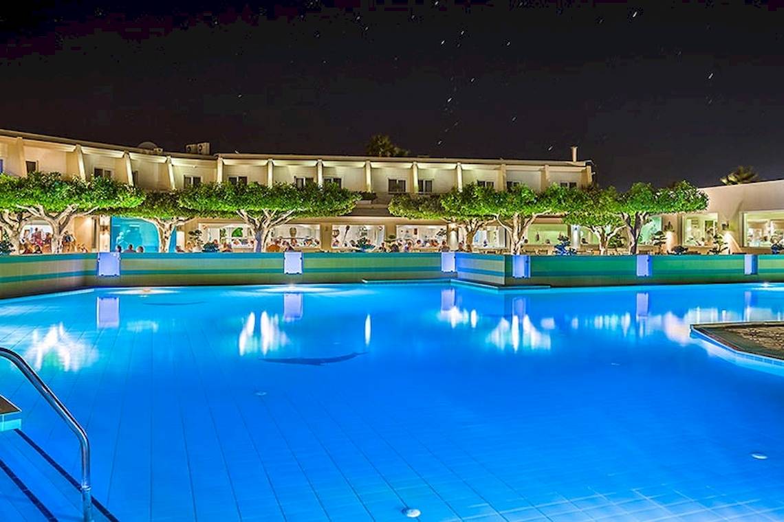 Nachtansicht des Swimmingpools des Sandy Beach Hotels auf Kos mit beleuchteten Gebäuden und Bäumen