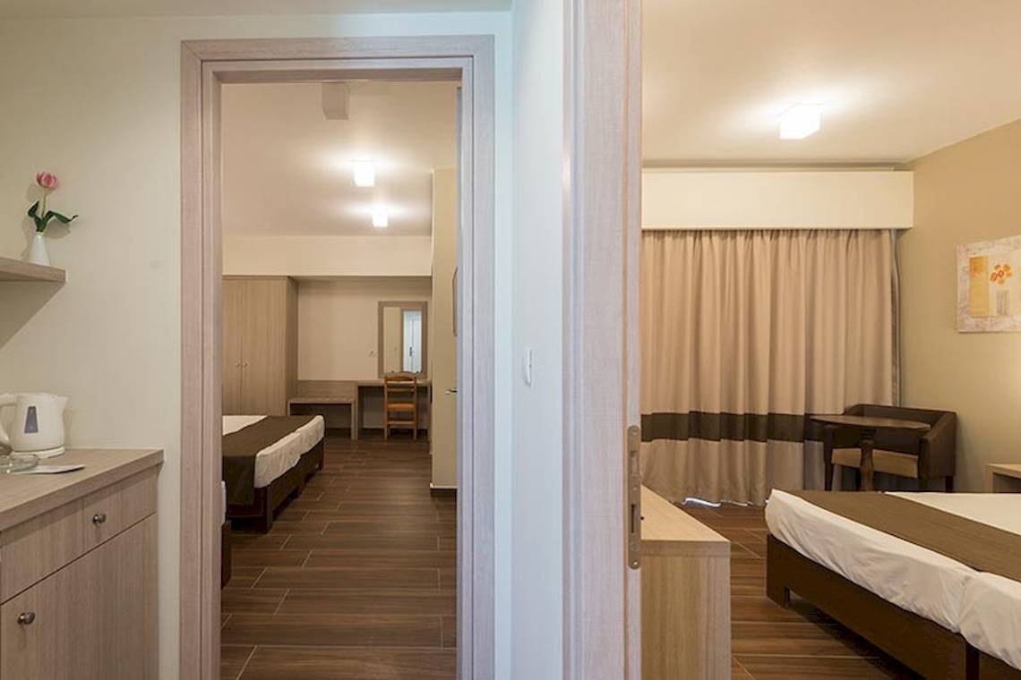 Innenansicht des Zimmers im Sandy Beach Hotel auf Kos mit zwei Betten, Tisch, Stuhl und Dekor.