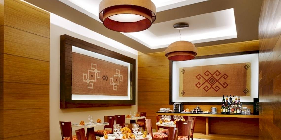Innenbereich des Barcelo Maya Beach Hotels mit gerahmten Wanddekorationen, runden Kronleuchtern, Holzmöbeln und einer Bar.