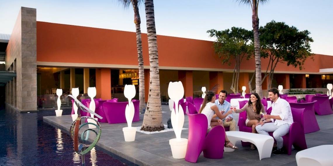 Vier Personen sitzen auf einem Außenbereich des Barcelo Maya Beach Hotels neben einem Pool.