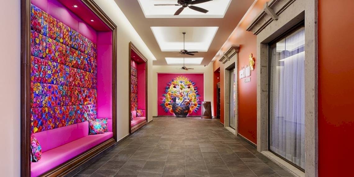 Der Innenbereich des Barcelo Maya Beach Hotels mit rosa Wänden, bunten Wandverkleidungen und einer zentralen Wandkunst.