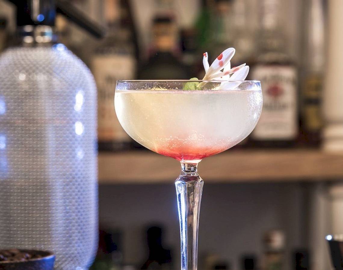 Ein Cocktail in einem Glas auf einer Bar mit einer Blume obenauf.