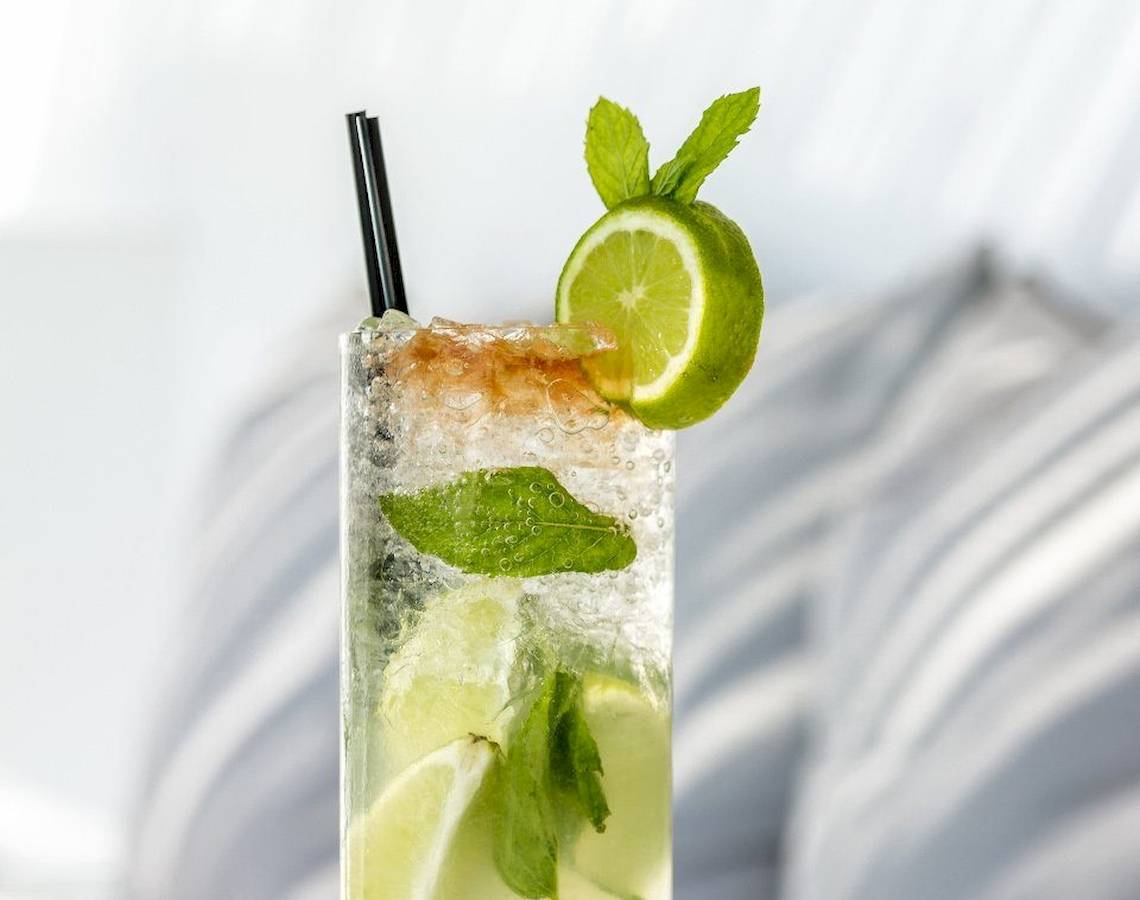 Ein Glas mit alkoholfreiem Cocktail, garniert mit Limetten und Minzblättern.