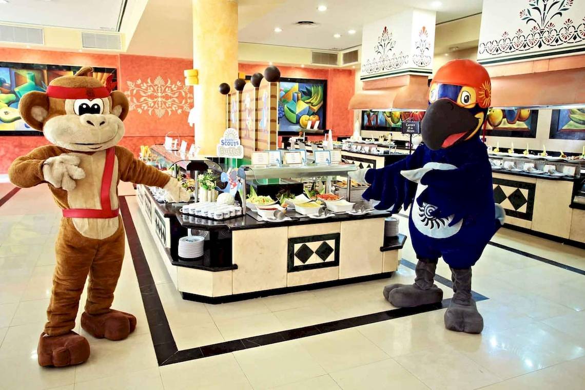 Zwei Maskottchen, ein Affe und ein Vogel, stehen vor einem Buffet im Bahia Principe Grand Coba Hotel.