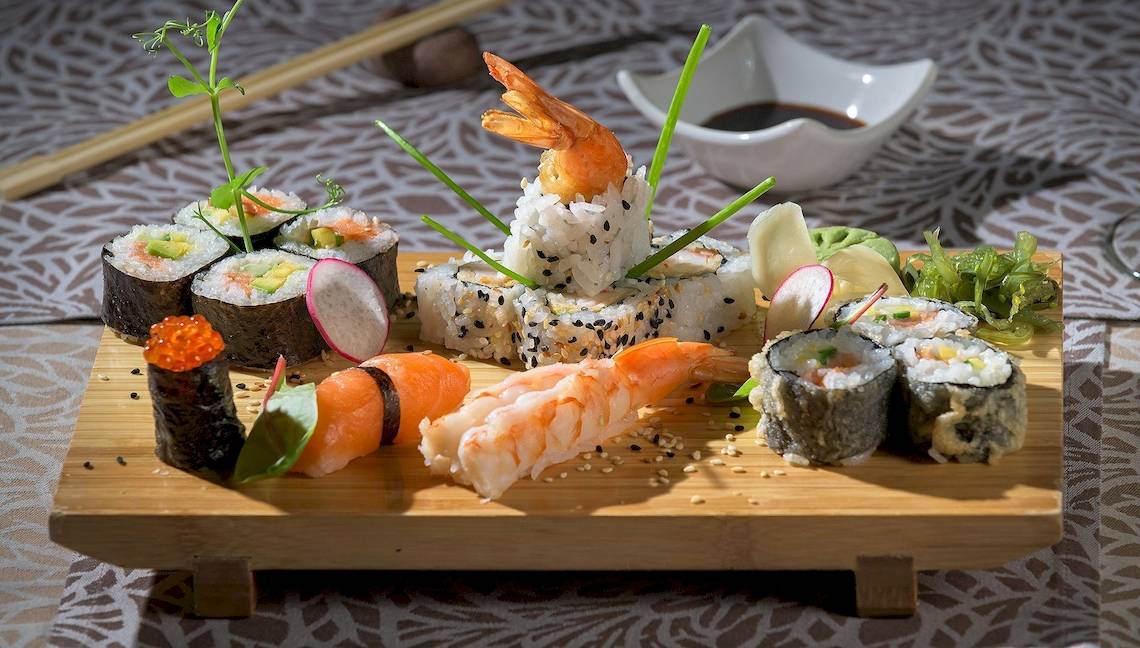 Ein Sushi-Platter mit verschiedenen Sushi-Rollen, Garnelen und Rettichscheiben auf einem Holzbrett.