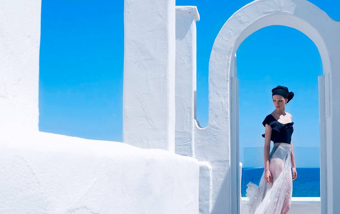 Frau in schwarzem Kleid vor weissen Mauer mit Meerblick im Knossos Beach Bungalows Suites Resort & Spa