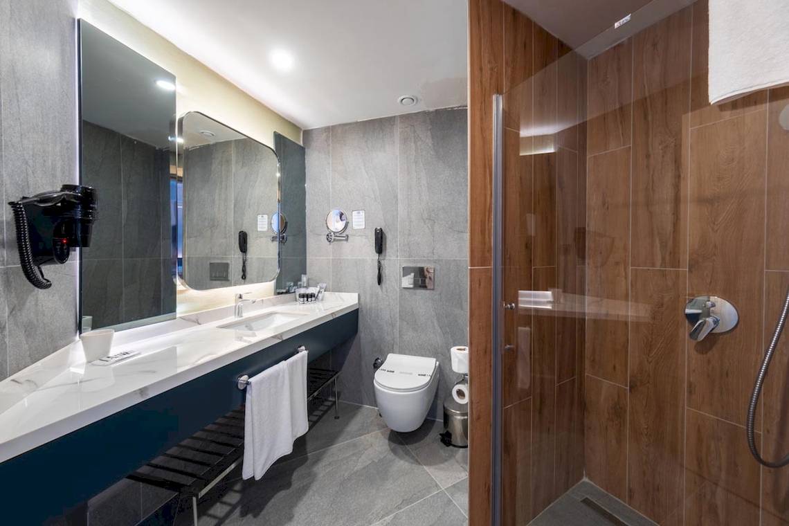 Badezimmer im Lago Hotel mit Marmorfliesen, blauer Waschtisch, Spiegel, Toilette und Duschkabine.