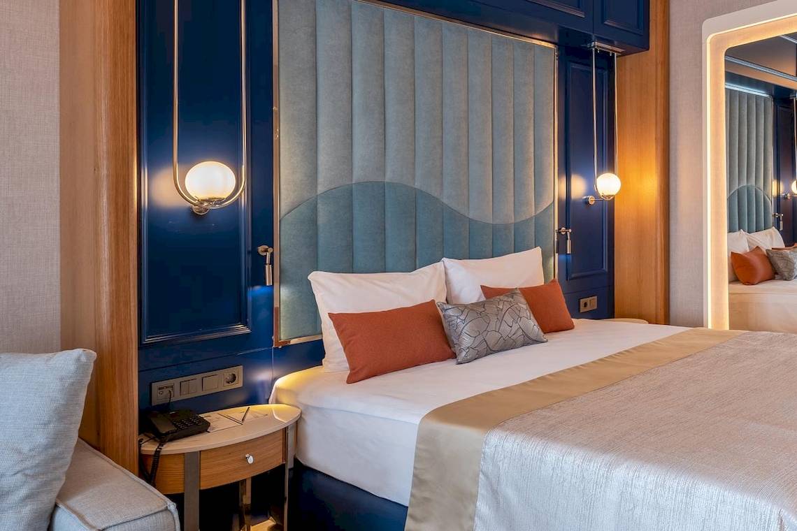 Bettzimmer im Lago Hotel mit blauen Wandverkleidungen, Kissen und Nachttisch