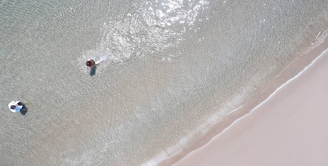 Zwei Personen stehen im klaren Wasser am Strand.
