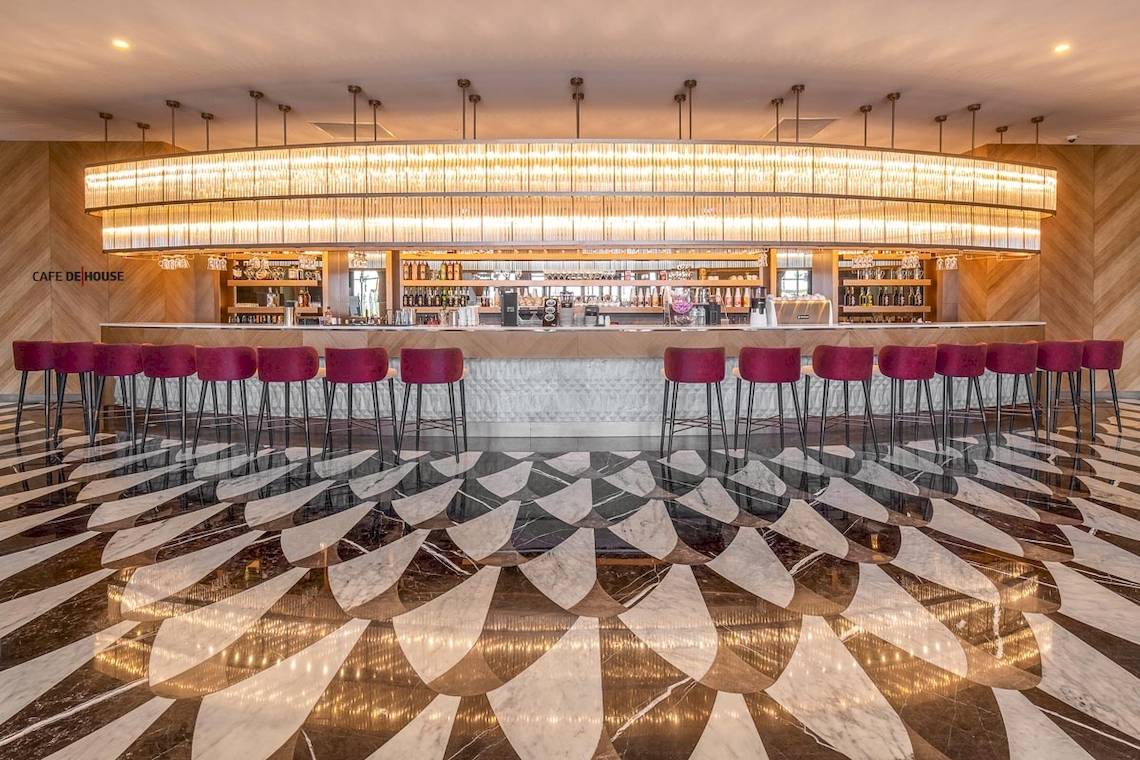 Café De House im Lago Hotel mit geometrischem Bodendesign und rote Stühle.
