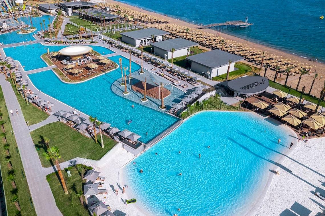 Luftaufnahme des Lago Hotels mit großen Swimmingpools, Sonnenschirmen und einem weißen Strand.