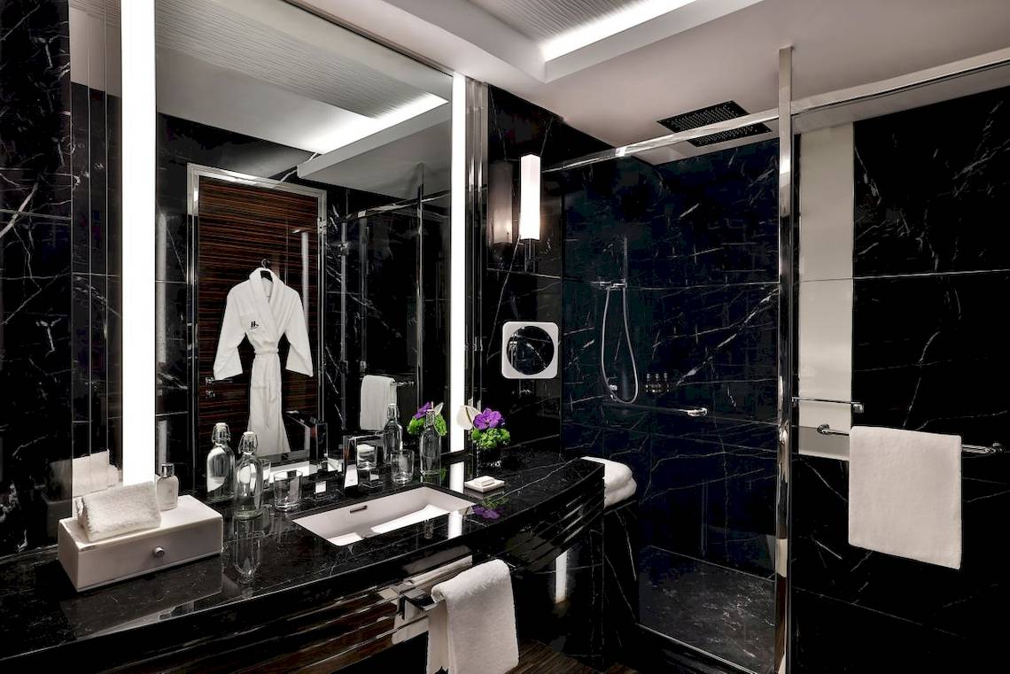 Luxuriöses Badezimmer im Marriott Resort Palm Jumeirah, Dubai, mit schwarzem Marmor, weißem Bademantel und frischen Blumen.