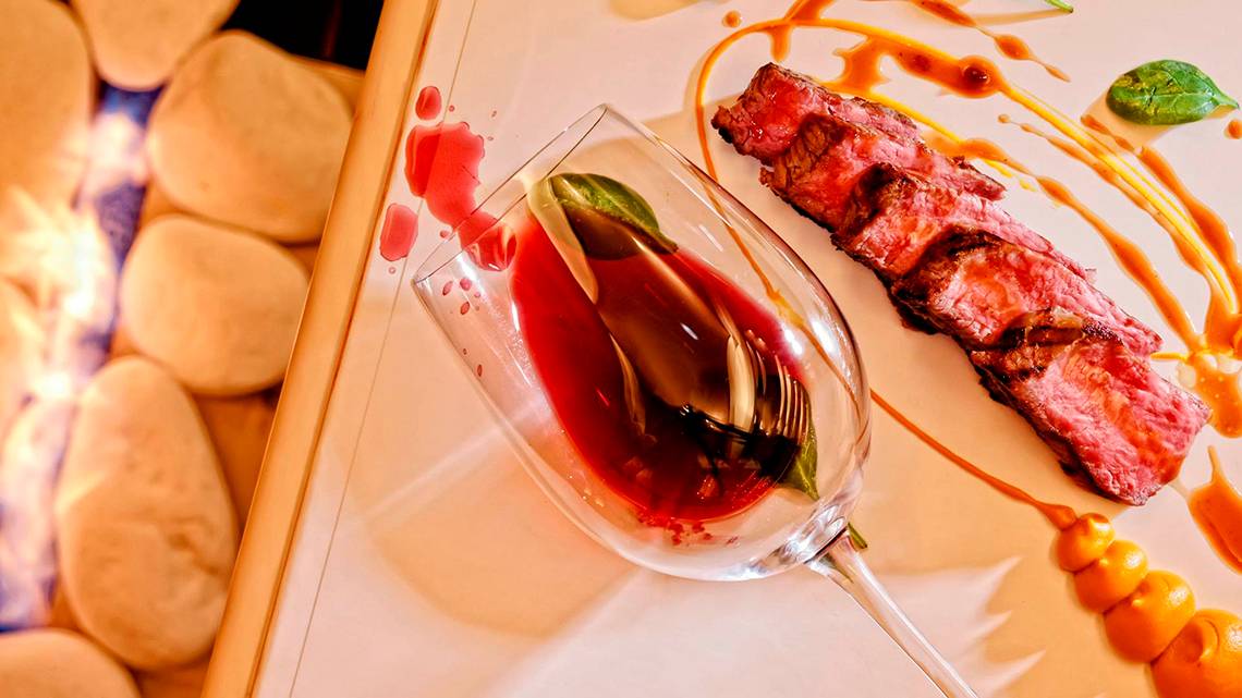 Ein Gericht mit Steak auf einem Teller, dazu ein Glas Wein, serviert im Knossos Beach Bungalows Suites Resort & Spa.