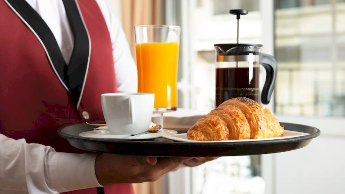Ein Kellner serviert Frühstück mit Croissant, Kaffee und Orangensaft im Grand Palace Hotel.