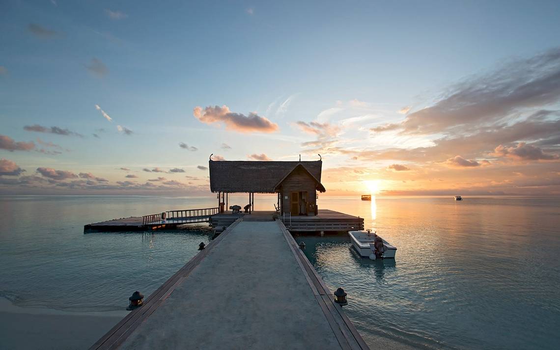 Sonnenuntergang über dem Constance Ephelia Hotel in Mahe, Seychellen, mit einer kleinen Hütte am Ende des Piers.