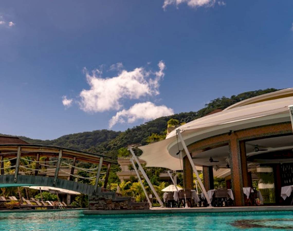 Außenpool des Savoy Seychelles Resort & Spa mit Brücke und Sonnenliegen.