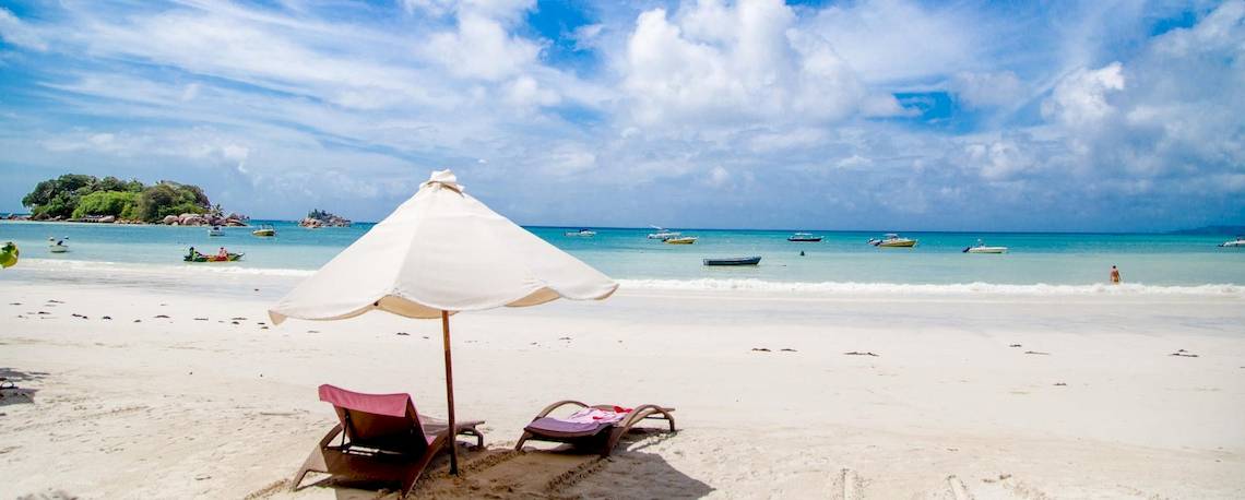 Strand mit Sonnenschirm und Liegen im Hintergrund befindet sich ein Hotel
