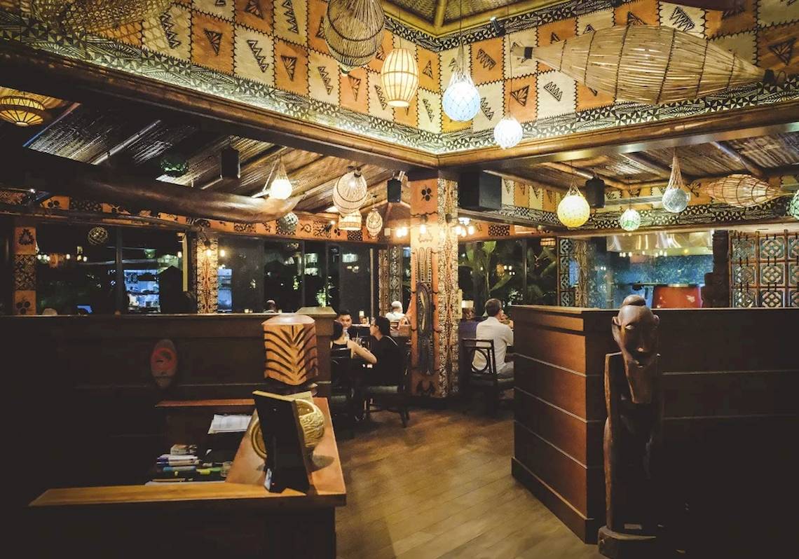Innenbereich des STORY Seychelles Hotels mit Holzboden, Holztischen und hängenden Lampen.