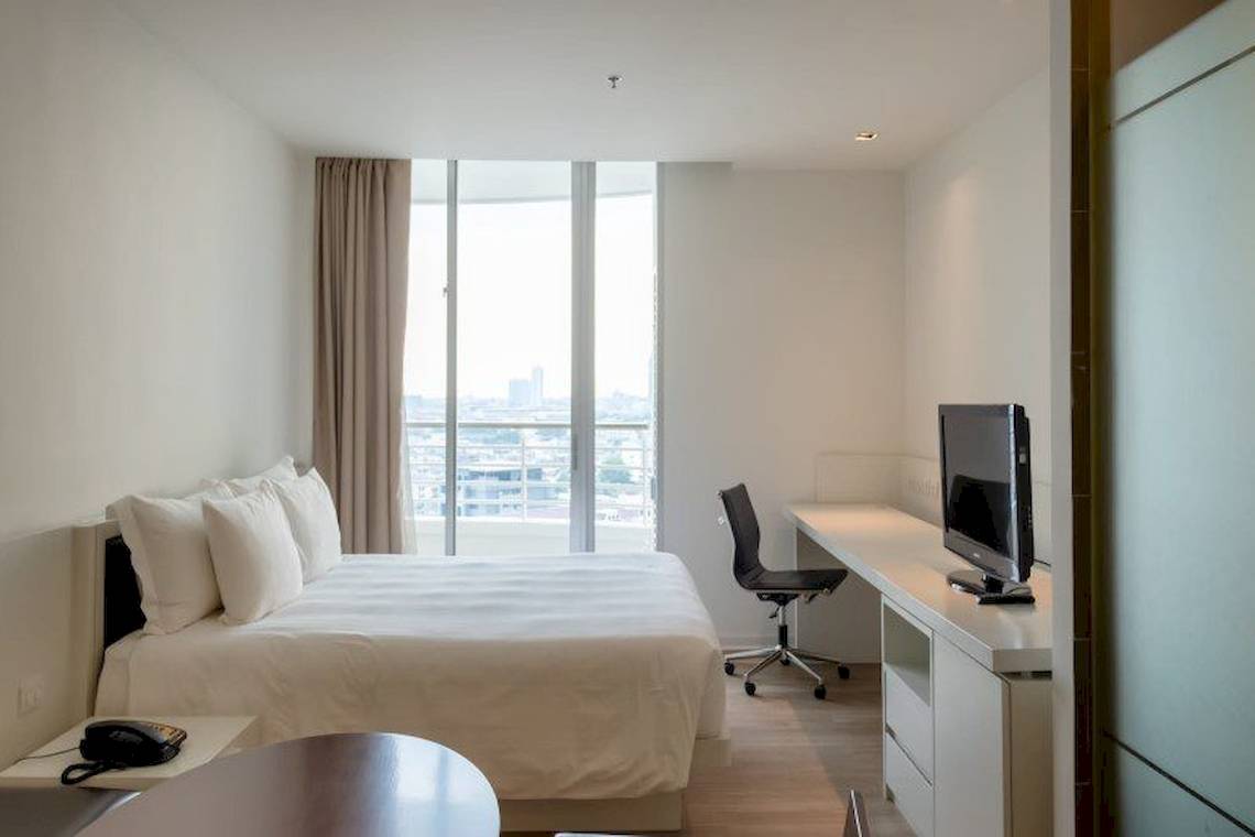Hotelzimmer im JC Kevin Sathorn Bangkok mit Bett, Schreibtisch und Fernseher.