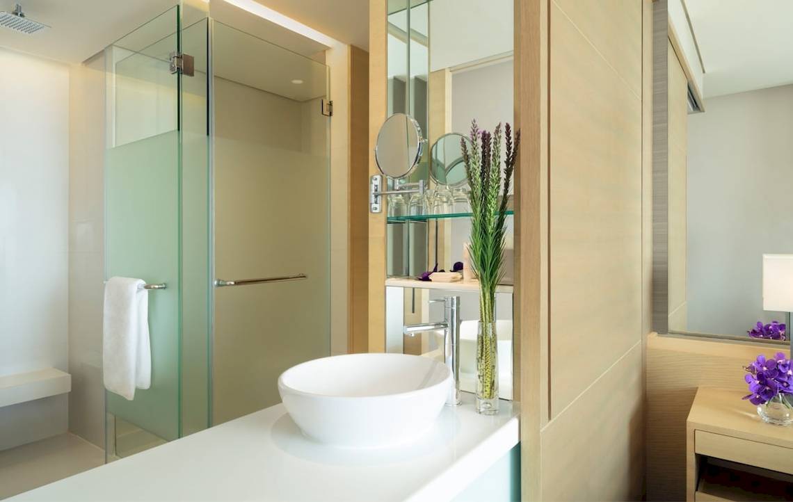 Badezimmer im AVANI+ Riverside Bangkok Hotel mit runden Waschbecken und Glasdusche.