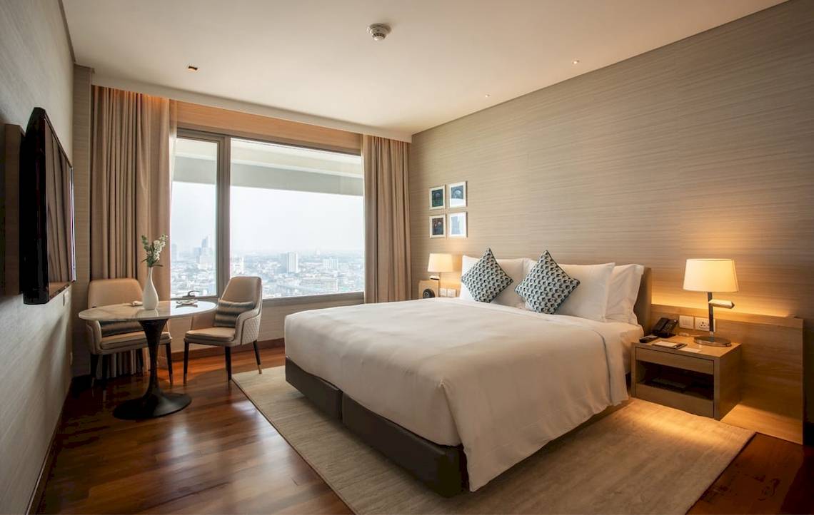 Innenansicht eines Zimmers im AVANI+ Riverside Bangkok Hotel mit großem Bett, Tisch und Blick auf die Stadt.
