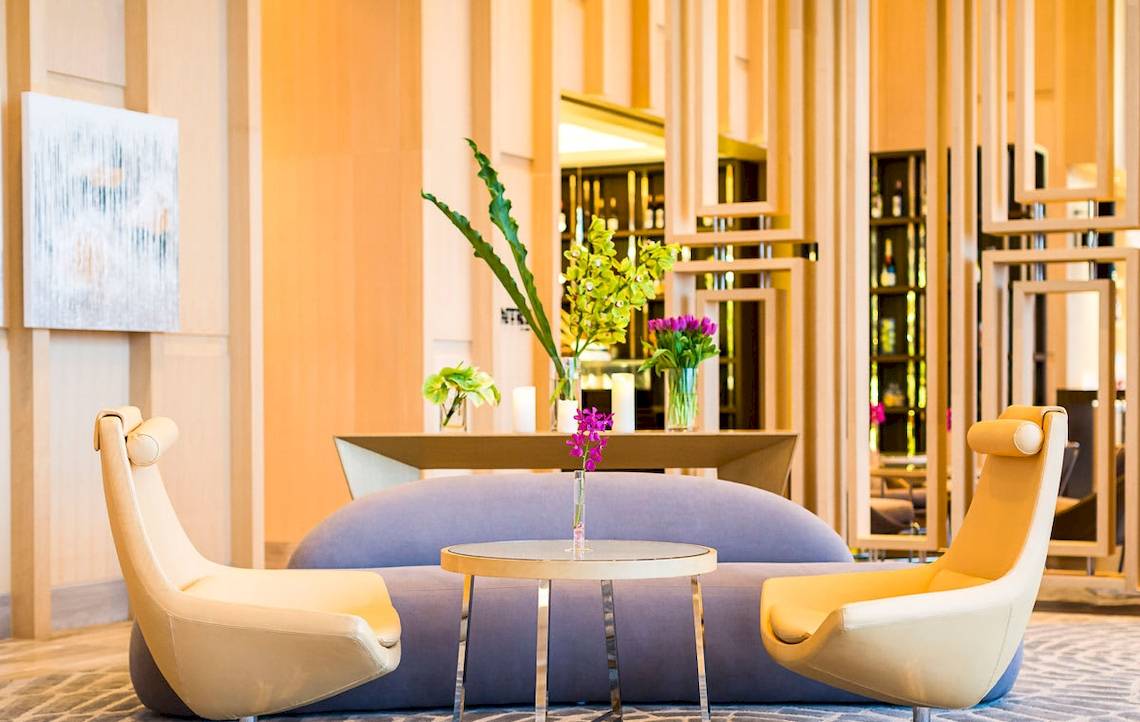 Lobby des AVANI+ Riverside Bangkok mit Sofas, Tisch, Blumen und moderner Einrichtung.