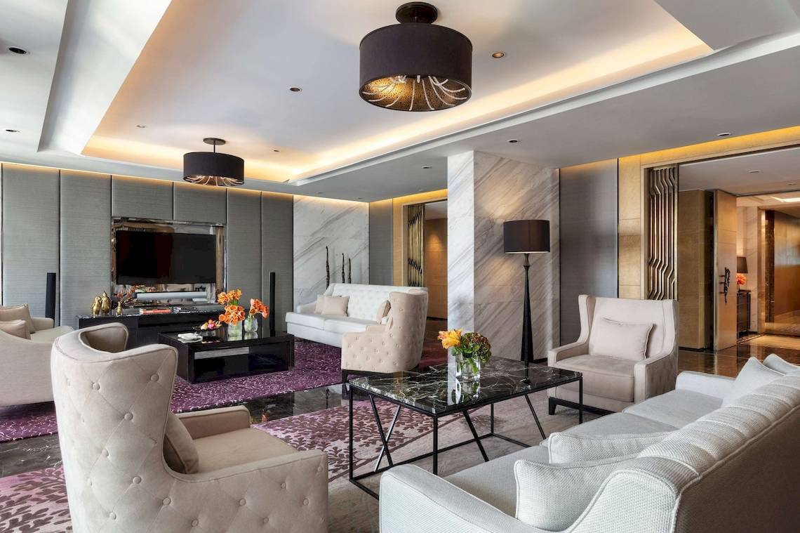 Wohnzimmer im Siam Kempinski Hotel Bangkok mit weißen Möbeln, einem Fernseher und Blumenvasen.