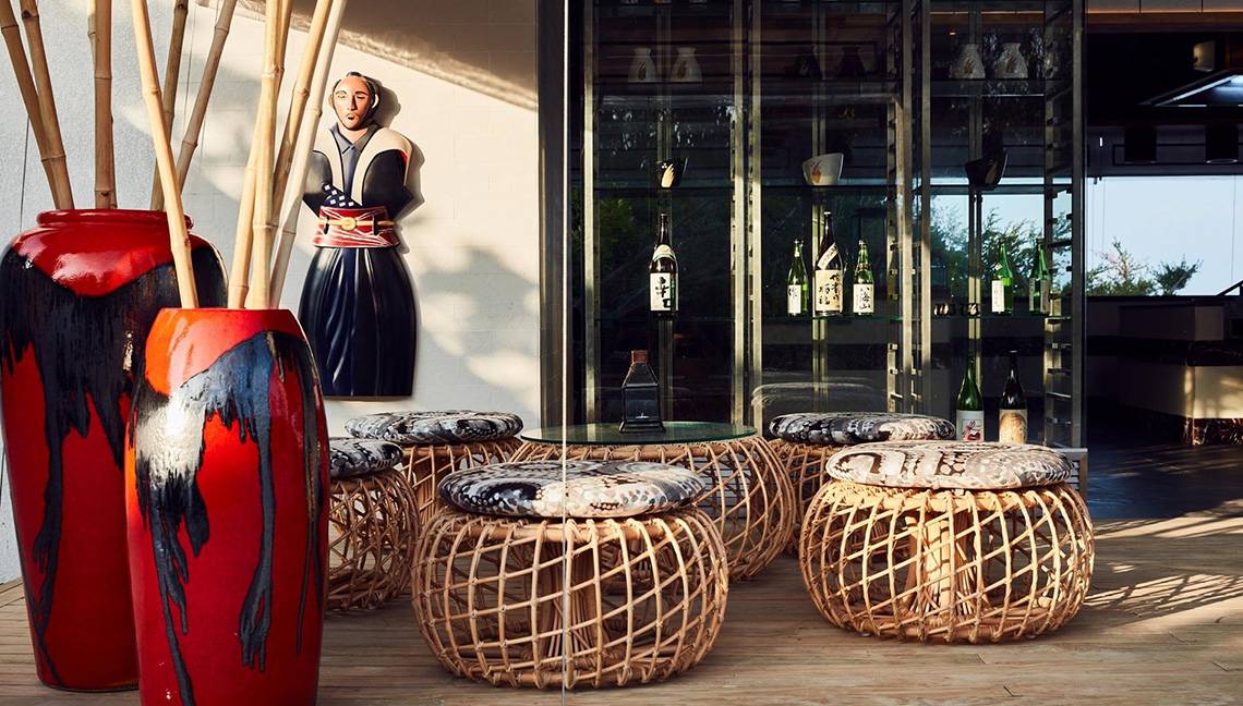 Hotellobby des Amari Havodda Maldives mit roten Vasen, Bambusstangen, Sitzhockern und einer Glasvitrine.