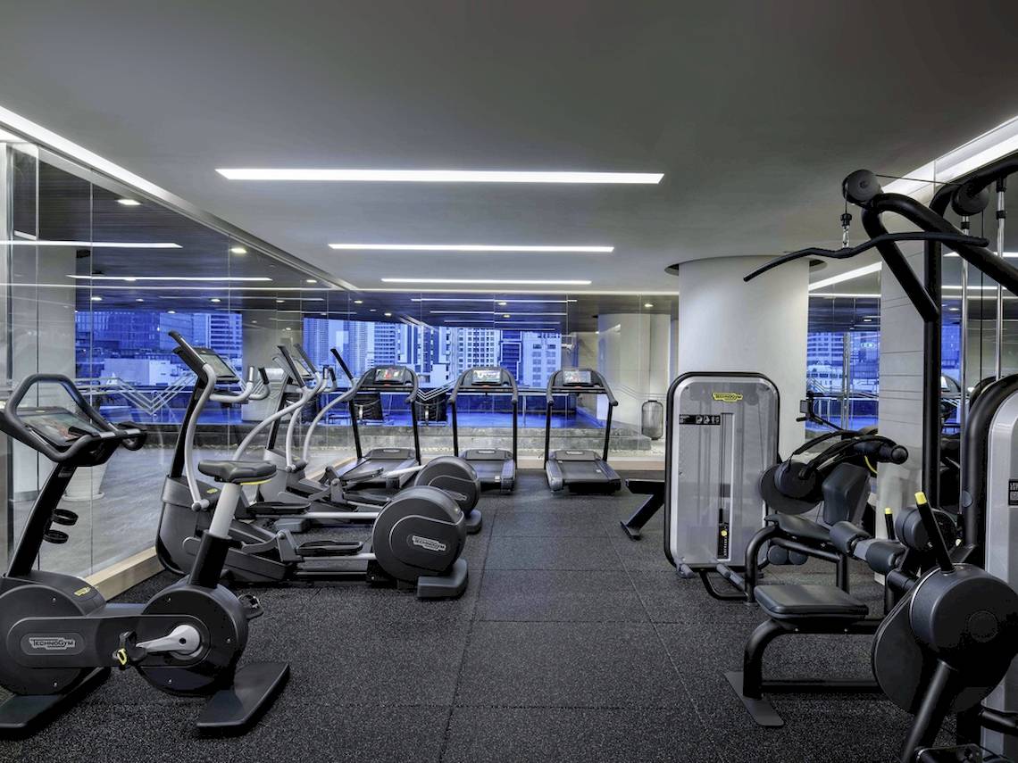 Fitnesscenter im Pullman Bangkok Hotel G mit verschiedenen Geräten und Ausblick auf die Stadt.